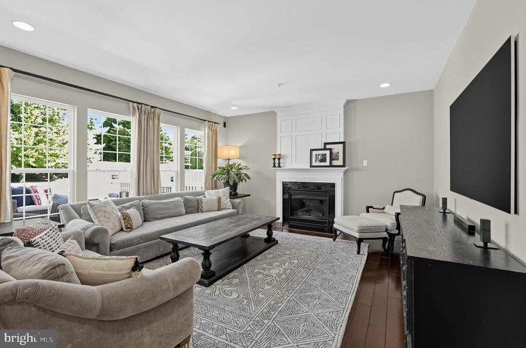 Furnished living room with a gray sectional, fireplace, large windows, and wall-mounted television.