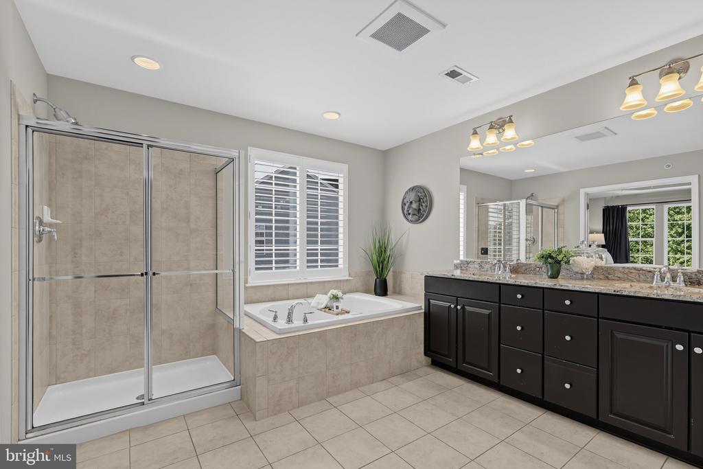 Primary bathroom with a tiled shower, soaking tub, and long dark double vanity.