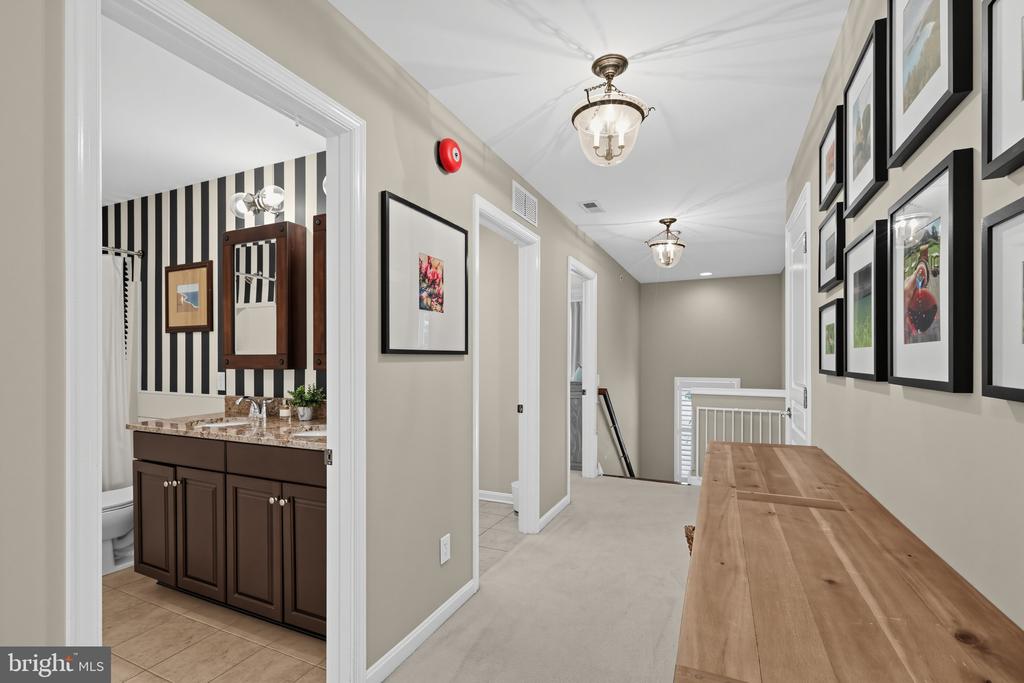 Upstairs hallway with framed artwork, a long wooden console table, and an adjoining bathroom.