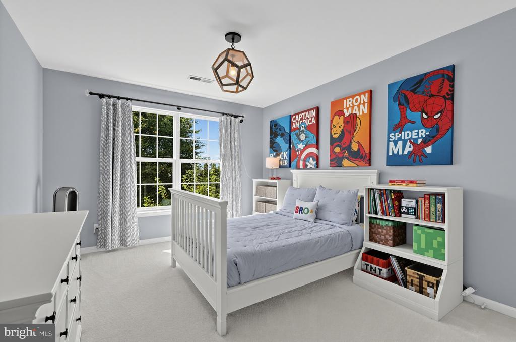 Bright bedroom with gray bedding, superhero posters, and a large window overlooking trees.
