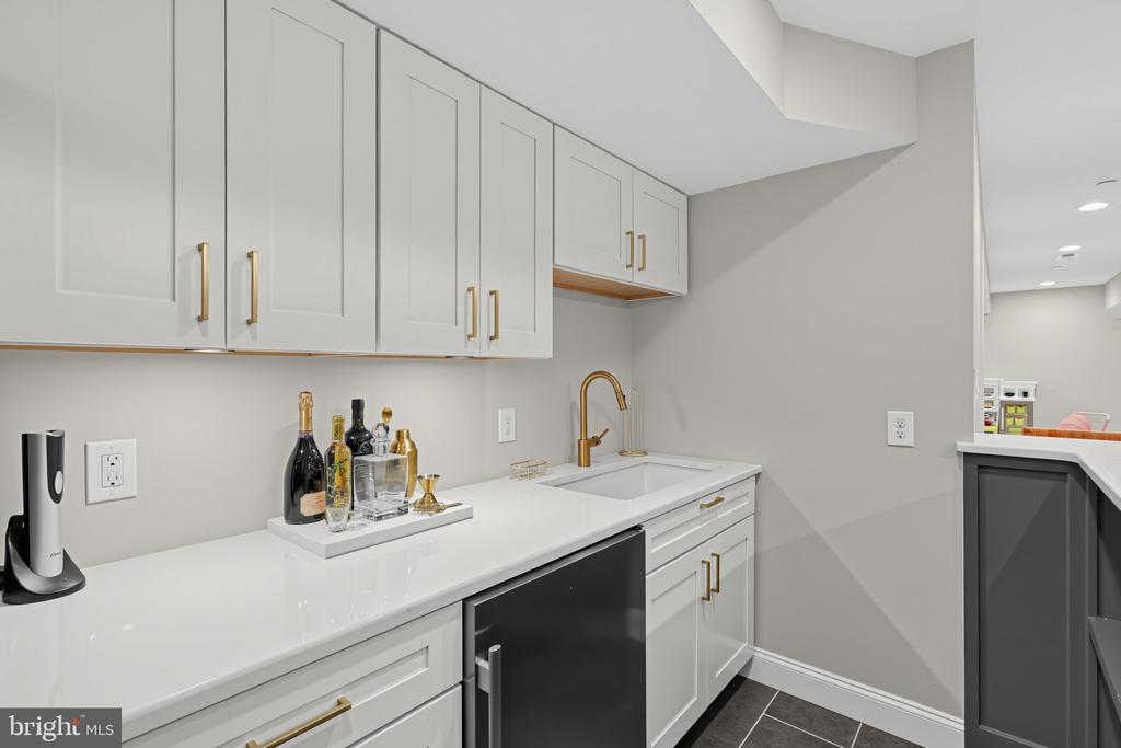 Wet bar with white cabinets, brass faucet, and black under-counter beverage refrigerator.