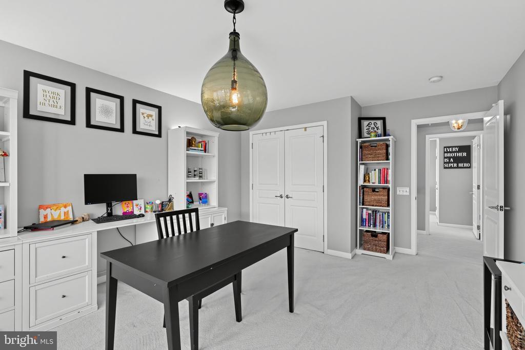 Home office with a large black desk, white built-ins, bookshelves, and a glass pendant light.