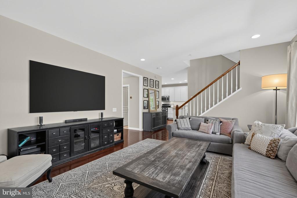 Living room with gray sofas, a patterned rug, and an open staircase beside the kitchen.