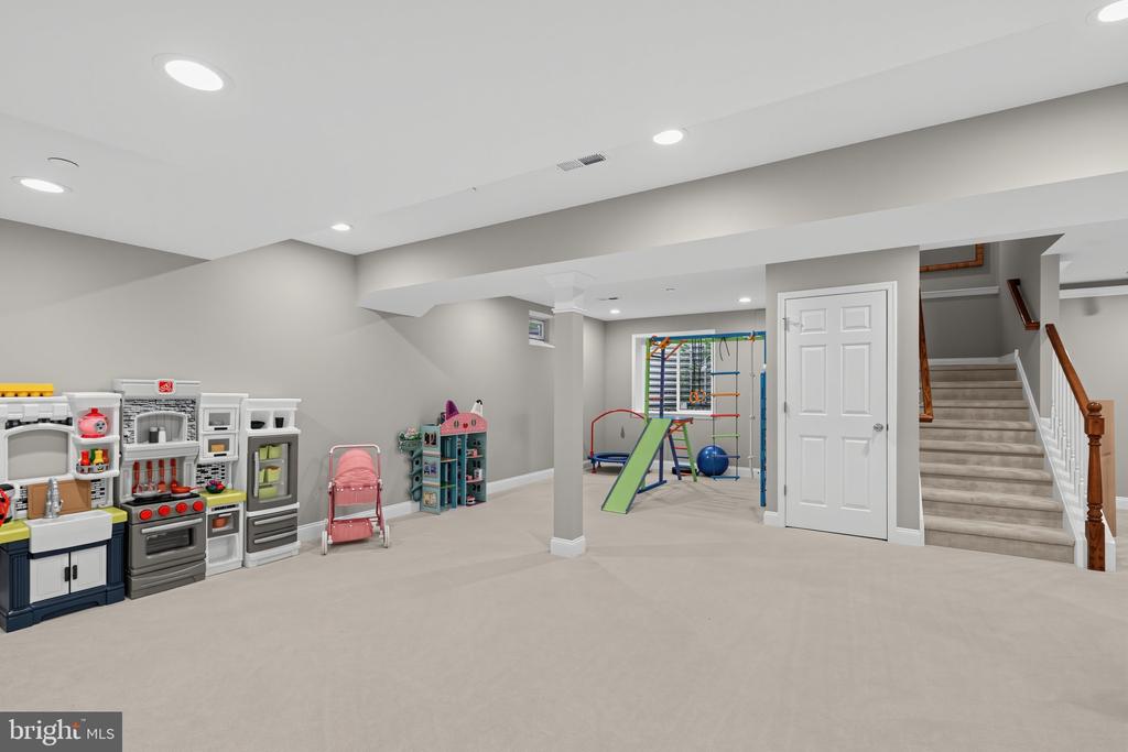Finished basement playroom with a toy kitchen, indoor climbing set, and carpeted stairs.