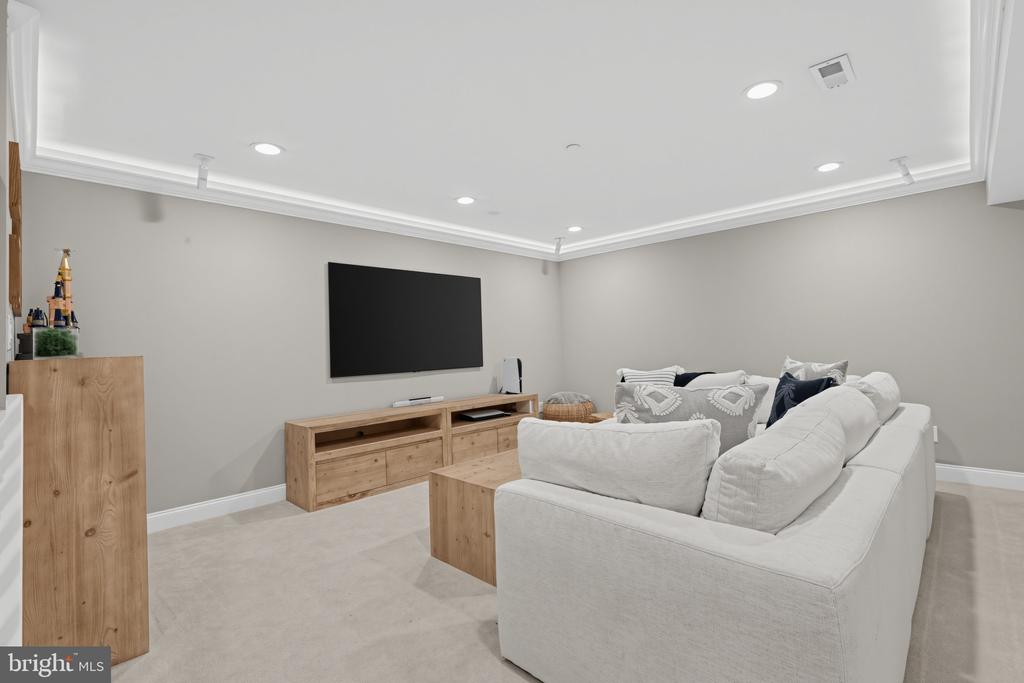 Living room with a white sectional sofa, wall-mounted television, and light wood media console.