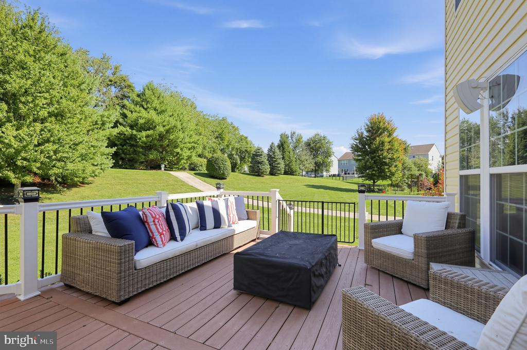 Furnished deck with wicker seating overlooks a broad lawn and mature trees.