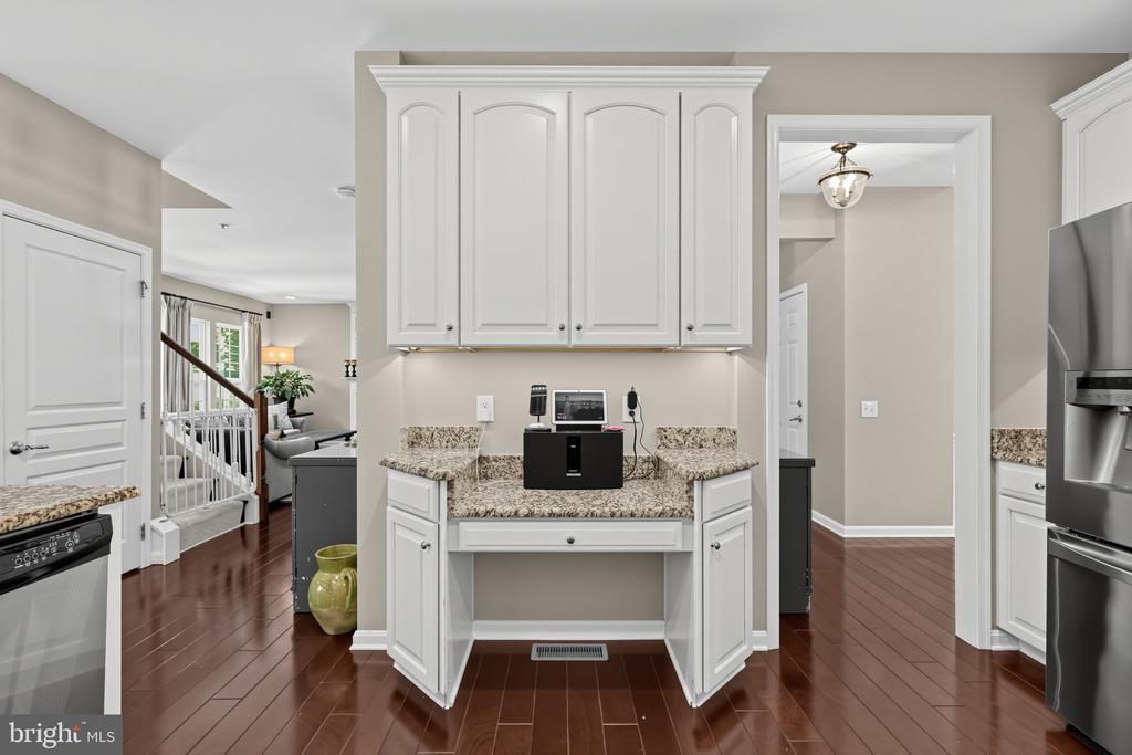Kitchen with white cabinetry, a built-in desk, granite countertops, and dark hardwood floors.