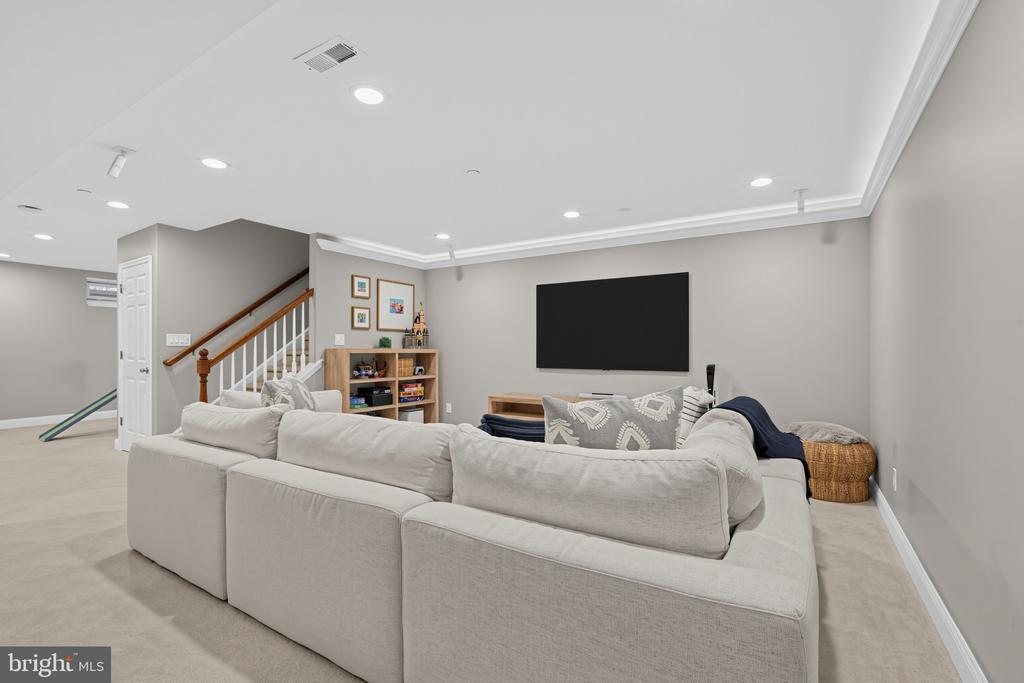 Basement family room with a large sectional sofa, wall-mounted television, and staircase.