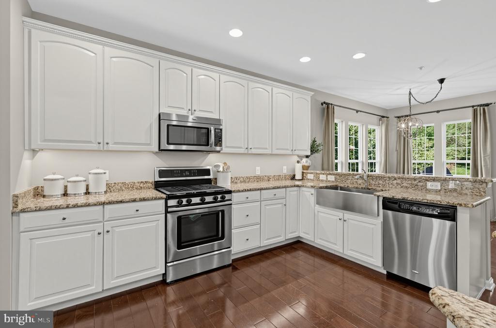 Kitchen with white cabinets, granite counters, stainless steel appliances, and dark hardwood floors.