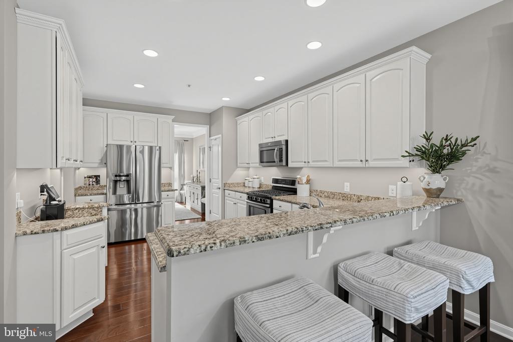 Kitchen with white cabinetry, granite breakfast bar, stainless steel appliances, and three upholstered stools.