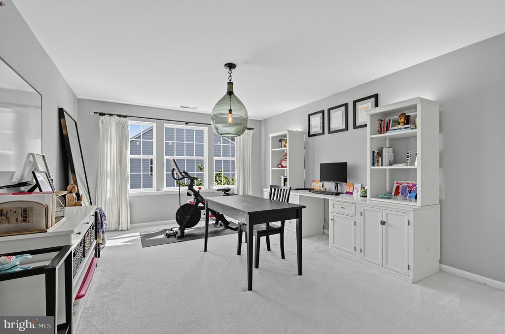 Home office with a black desk, white built-in cabinets, and a stationary bike by large windows.