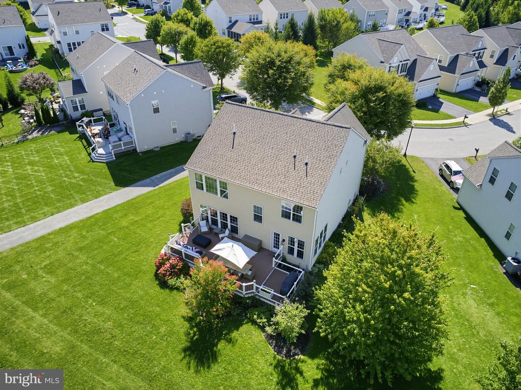 Rear of a two-story home with a deck and umbrella, surrounded by a broad lawn and neighboring houses.