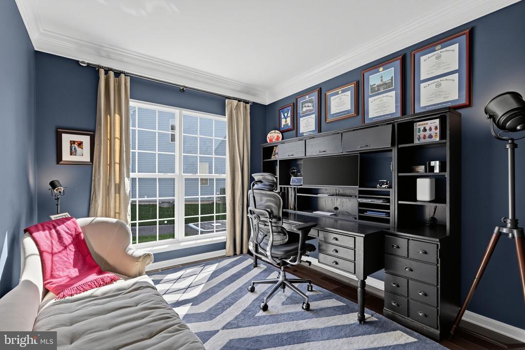 Furnished home office with built-in desk, framed certificates, and a daybed beside a large window.