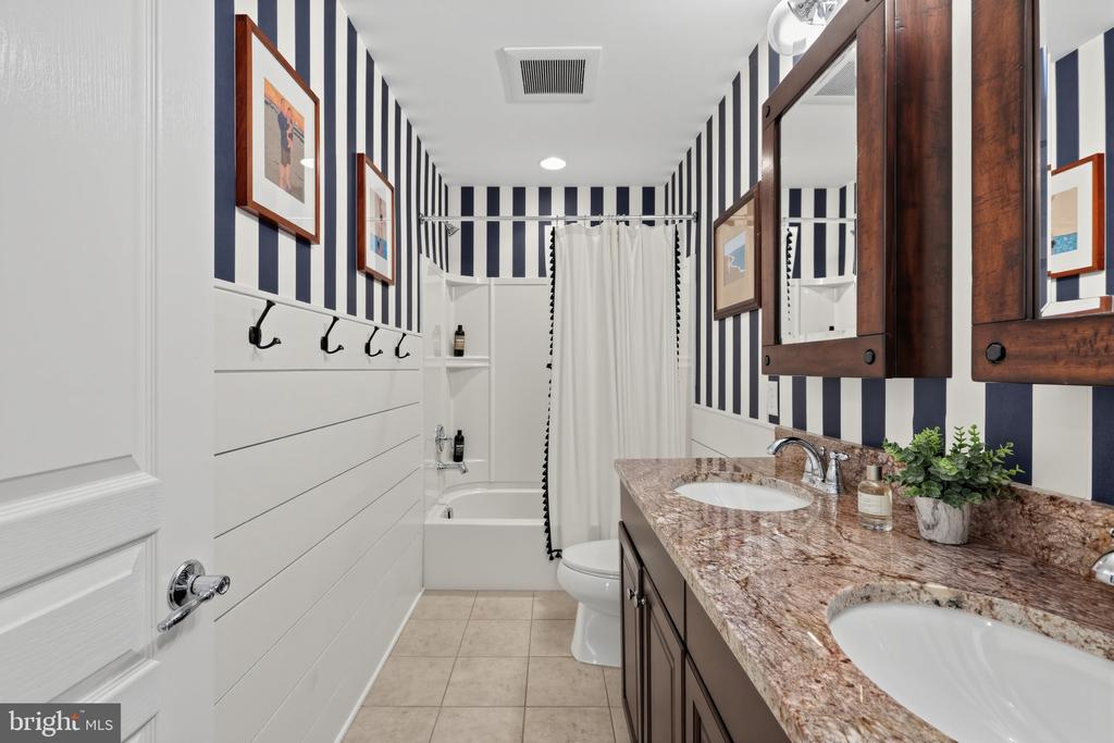 Bathroom with striped walls, a curtained bathtub, and a double-sink stone vanity.