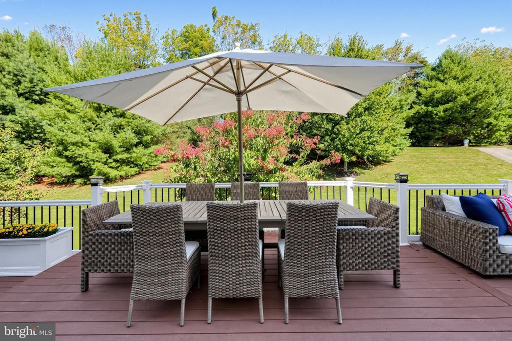 Deck dining area beneath a large white umbrella, overlooking a landscaped lawn and trees.