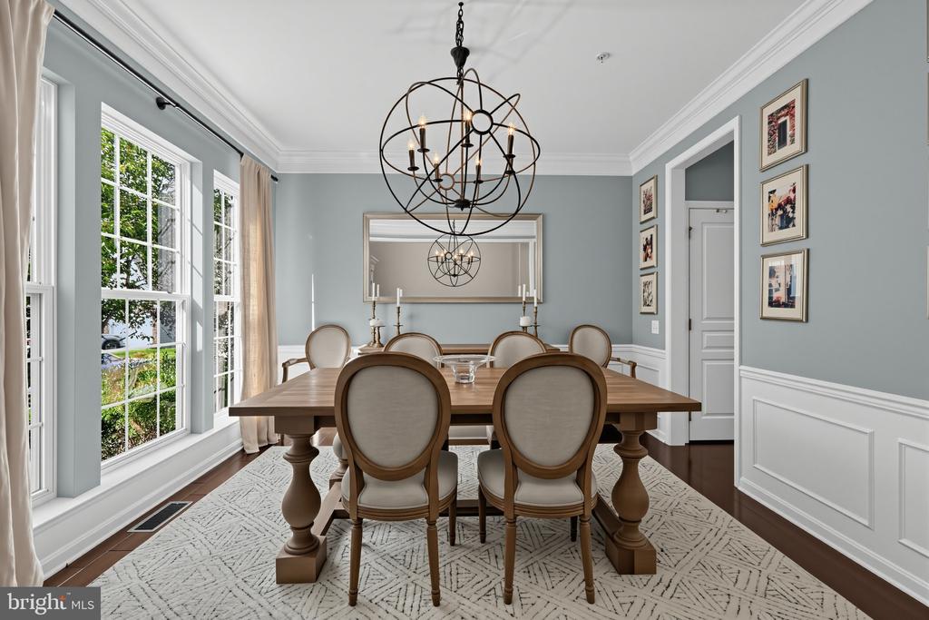 Dining room with a wooden table, upholstered chairs, large windows, and black orb chandeliers.