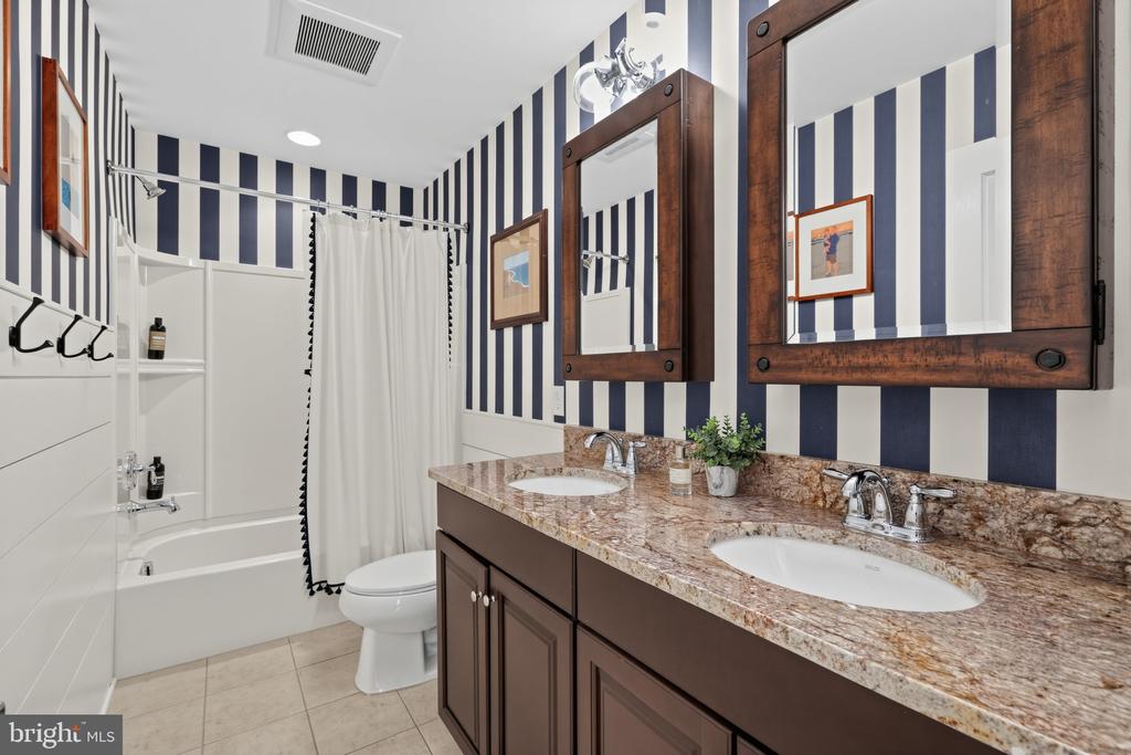 Bathroom with a double-sink wood vanity, stone countertop, and bold striped walls.