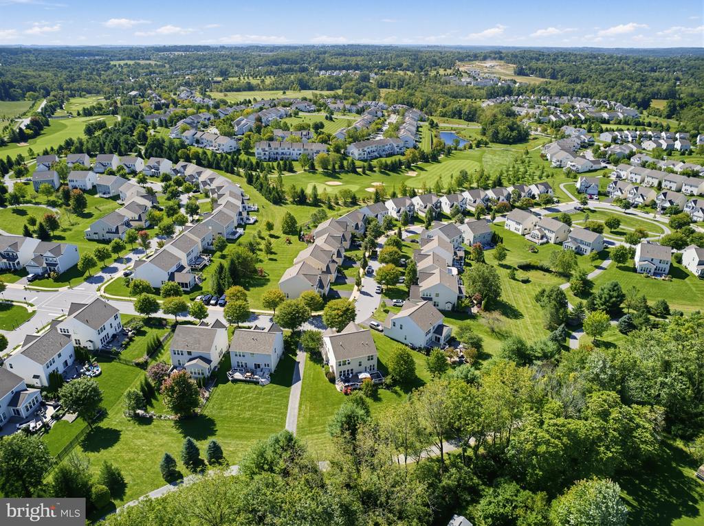 Aerial view of a suburban neighborhood with detached homes, landscaped lawns, and wooded surroundings.