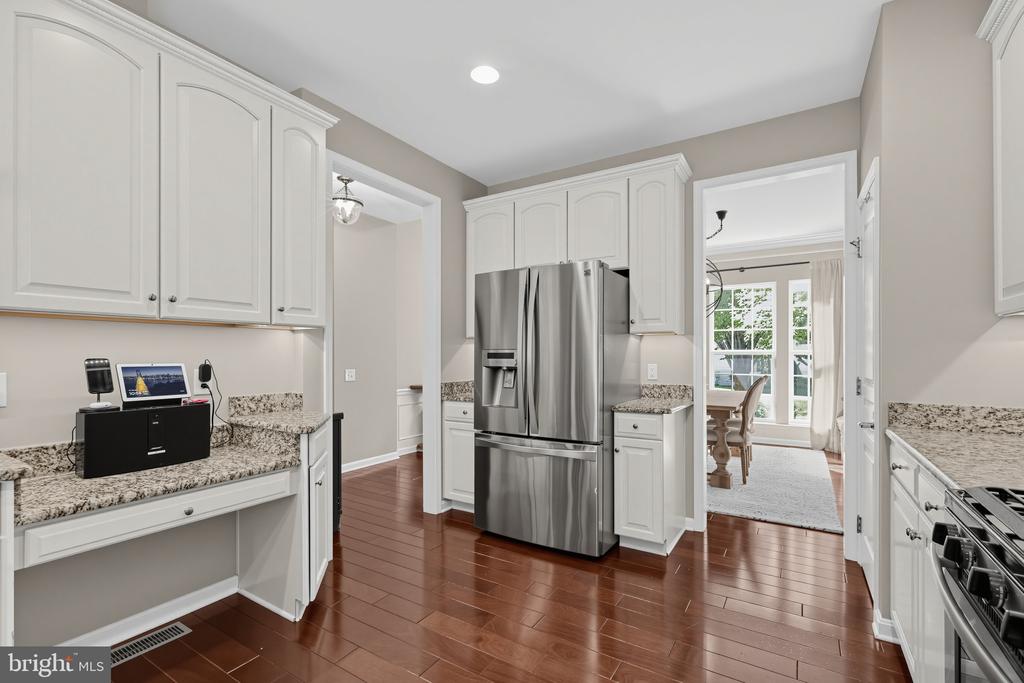 Kitchen with white cabinetry, granite counters, stainless steel refrigerator, and hardwood floors.
