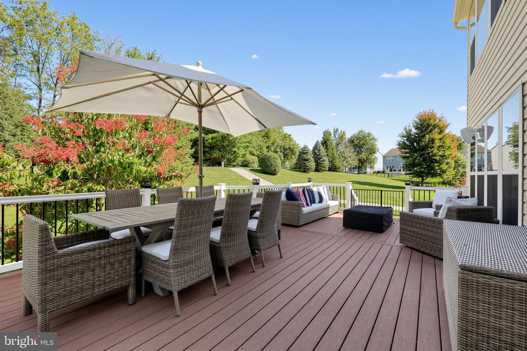 Furnished deck with umbrella and wicker seating overlooking a landscaped lawn.