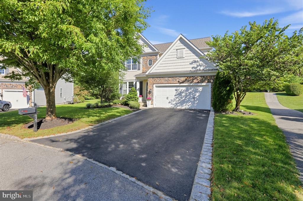 Two-story home with a stone facade, attached two-car garage, and tree-lined driveway.