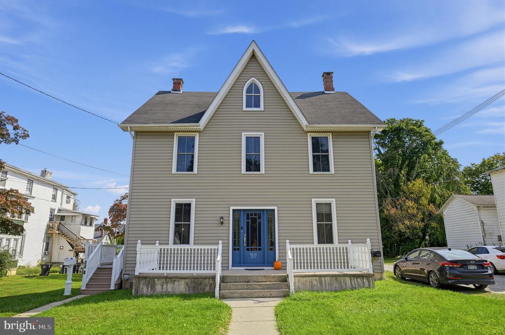 Two-story beige house with a steep central gable, blue front door, and white porch railings.