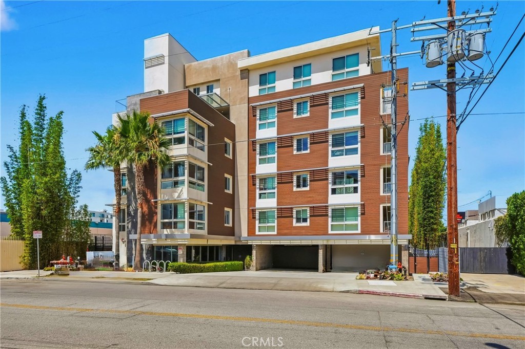 Modern multi-story apartment building with reddish-brown facade, balconies, and palm trees.