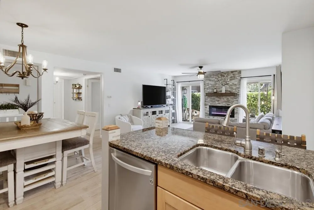 Open-plan kitchen with a granite island and sink overlooking the living room and stone fireplace.