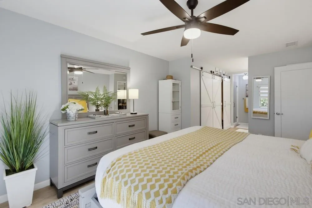 Bedroom with a mustard-yellow patterned runner, gray dresser, sliding barn doors, and ceiling fan.