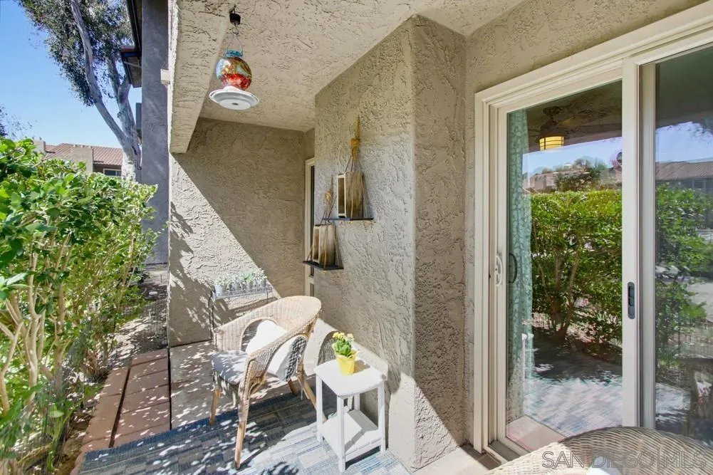 Furnished condo patio with wicker chairs, a small table, and hedges beside a sliding glass door.