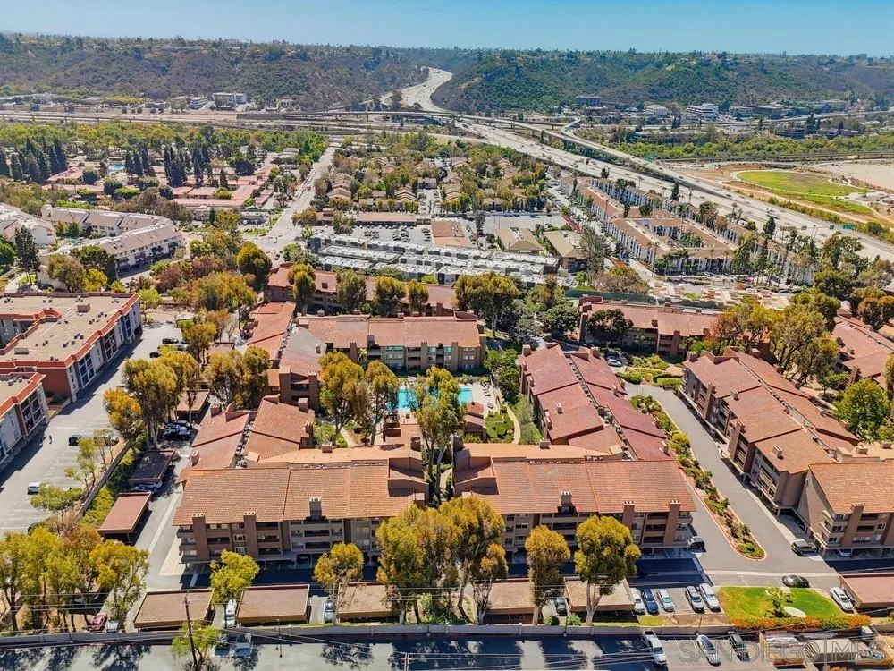 Aerial view of a condominium complex with red-tile roofs, a central pool, and freeway interchanges nearby.