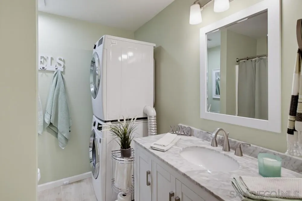 Bathroom vanity with a large mirror beside a stacked washer and dryer.