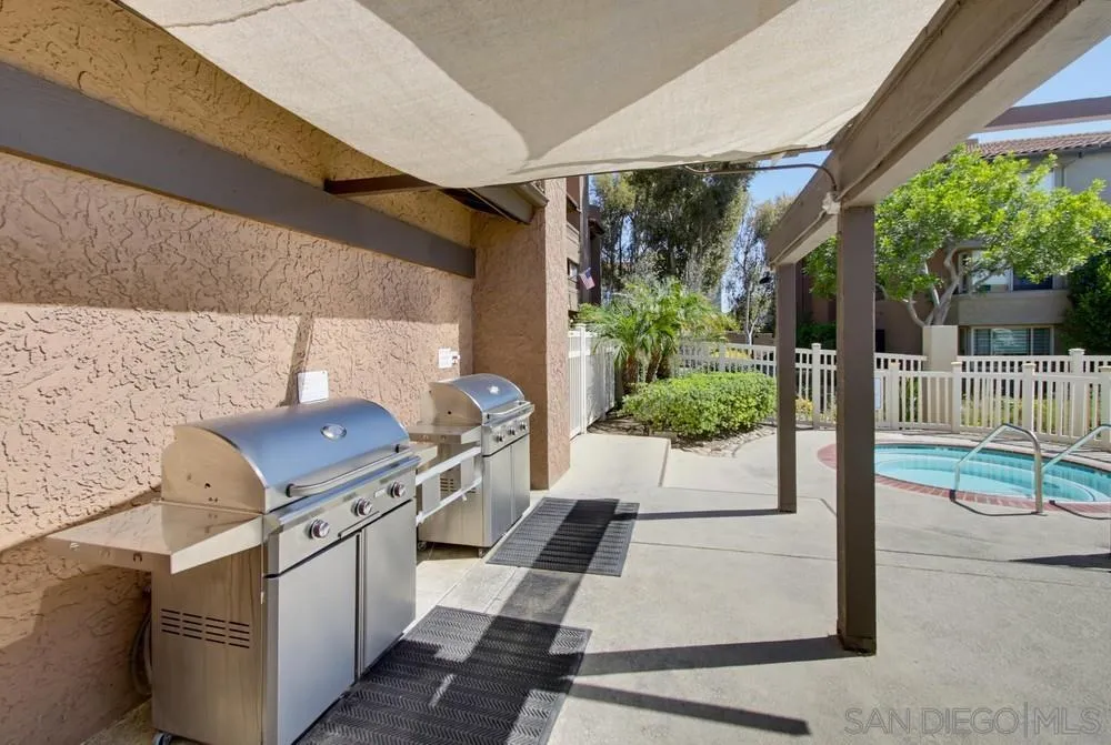 Covered patio with two stainless steel grills beside a fenced swimming pool.