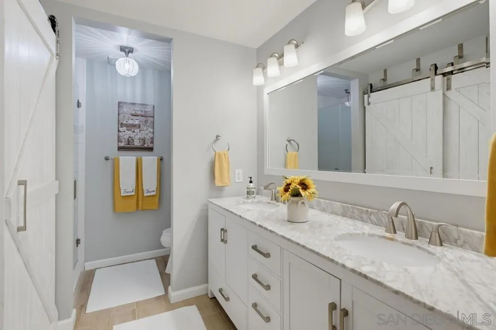 Bathroom with a long double vanity, marble-look counter, large mirror, and white sliding barn door.