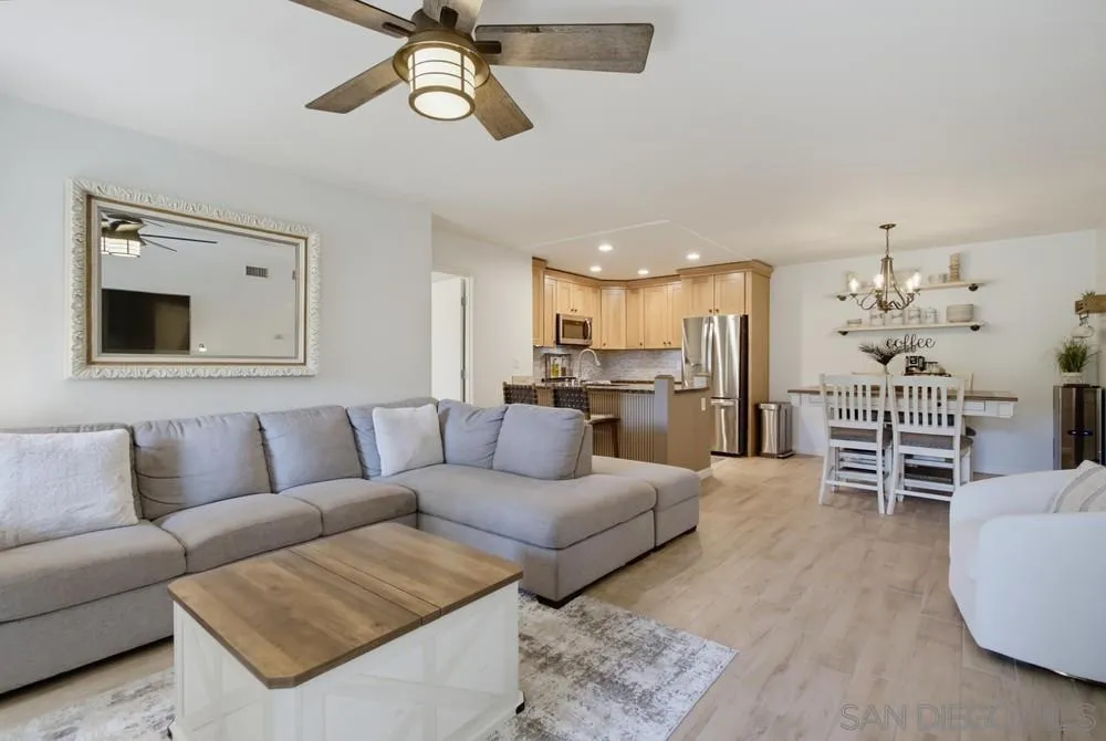 Open-plan living room with a gray sectional, wood coffee table, and adjoining kitchen and dining area.