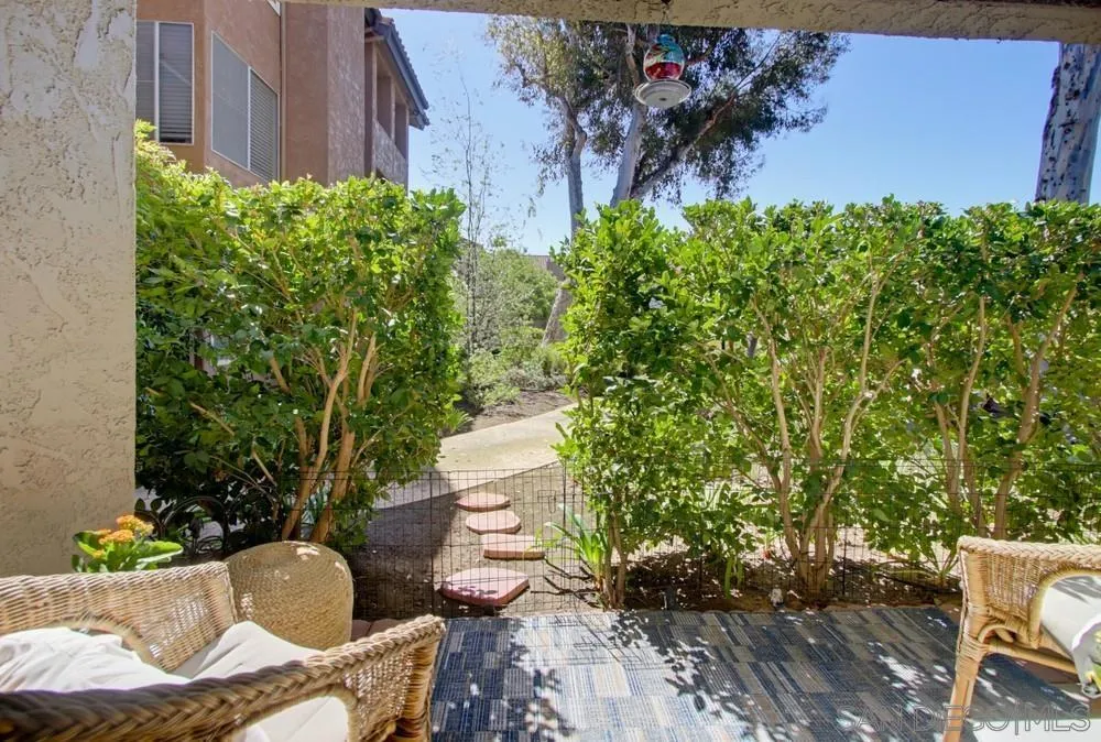 Covered patio with wicker seating and a stepping-stone path through leafy hedges.