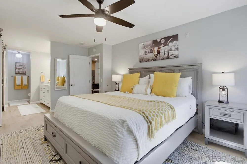 Staged bedroom with a large gray bed, yellow accent pillows, and a ceiling fan.