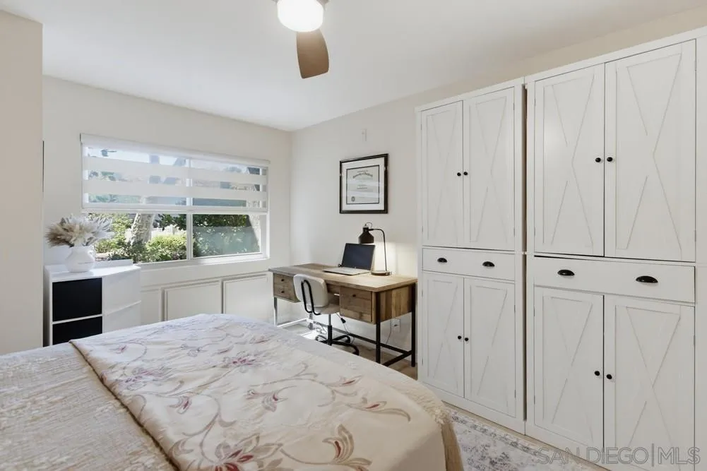 Bedroom with built-in white cabinets and a desk beside a window overlooking greenery.