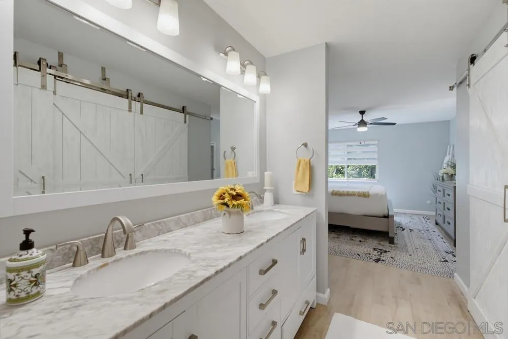 Bathroom vanity with marble-look counter and brass fixtures opening onto a bedroom.