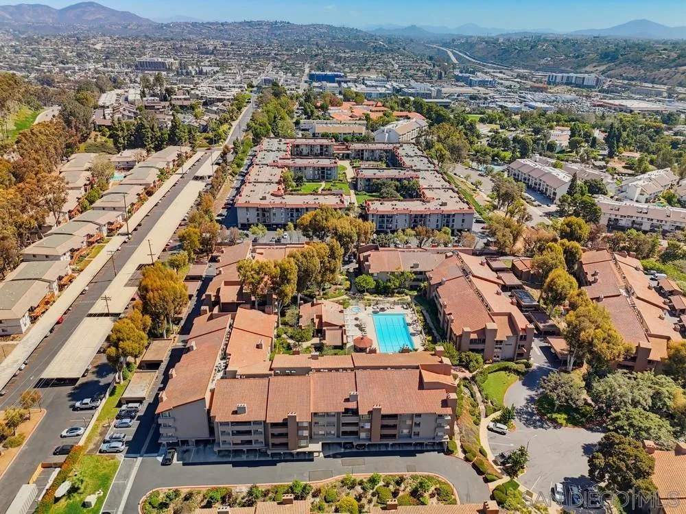 Aerial view of a condominium complex with a central swimming pool and mountains in the distance.