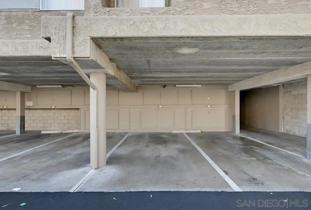 Covered parking spaces beneath a concrete ceiling with storage doors along the back wall.
