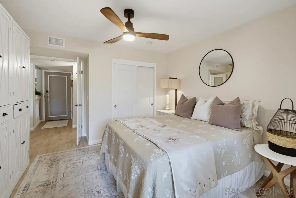 Staged bedroom with pale floral bedding, built-in white cabinets, and a wood-blade ceiling fan.