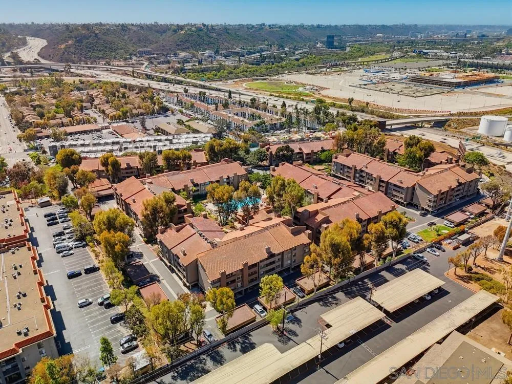 Aerial view of a condominium complex with red tile roofs, a pool, and surrounding hills.