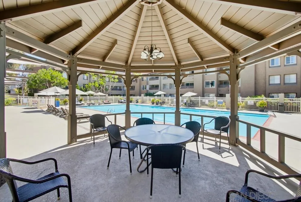 Community pool beside a shaded gazebo patio with a round table and chairs.