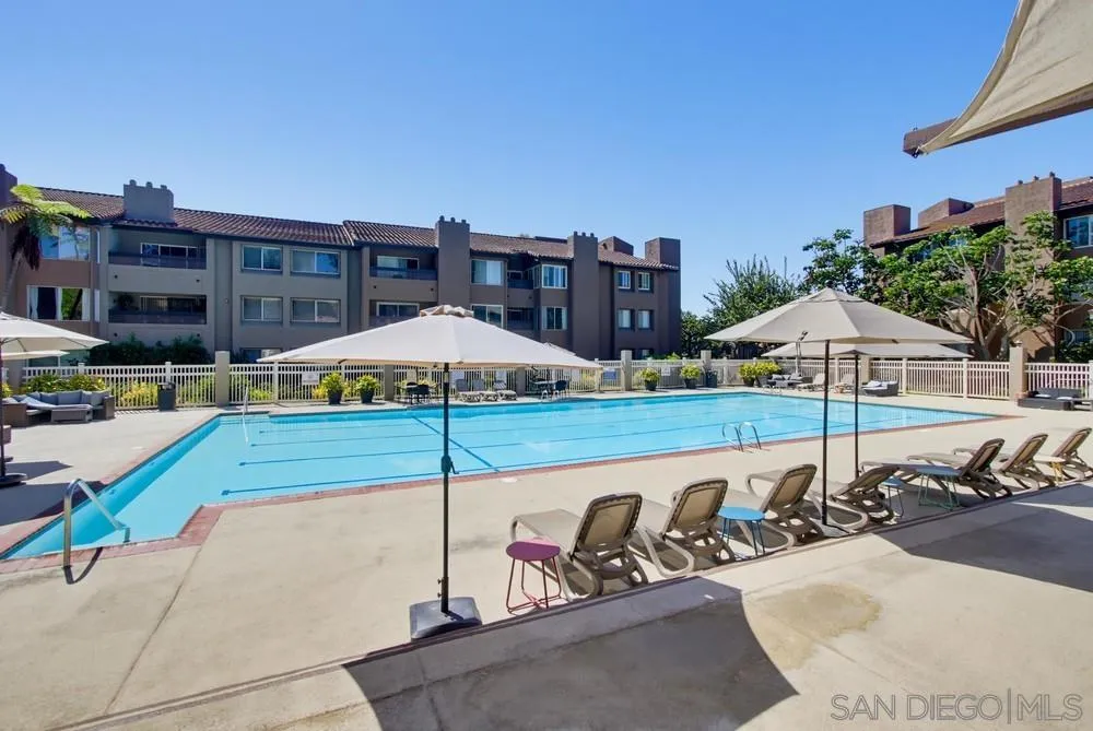 Condominium pool with lounge chairs and umbrellas in front of multistory residential buildings.