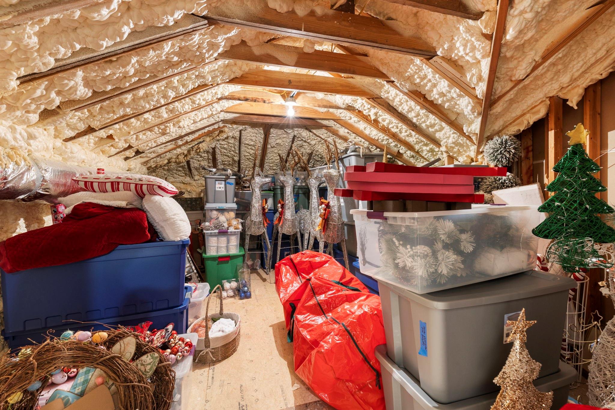 Attic storage area with exposed rafters, spray-foam insulation, and bins of holiday decorations.