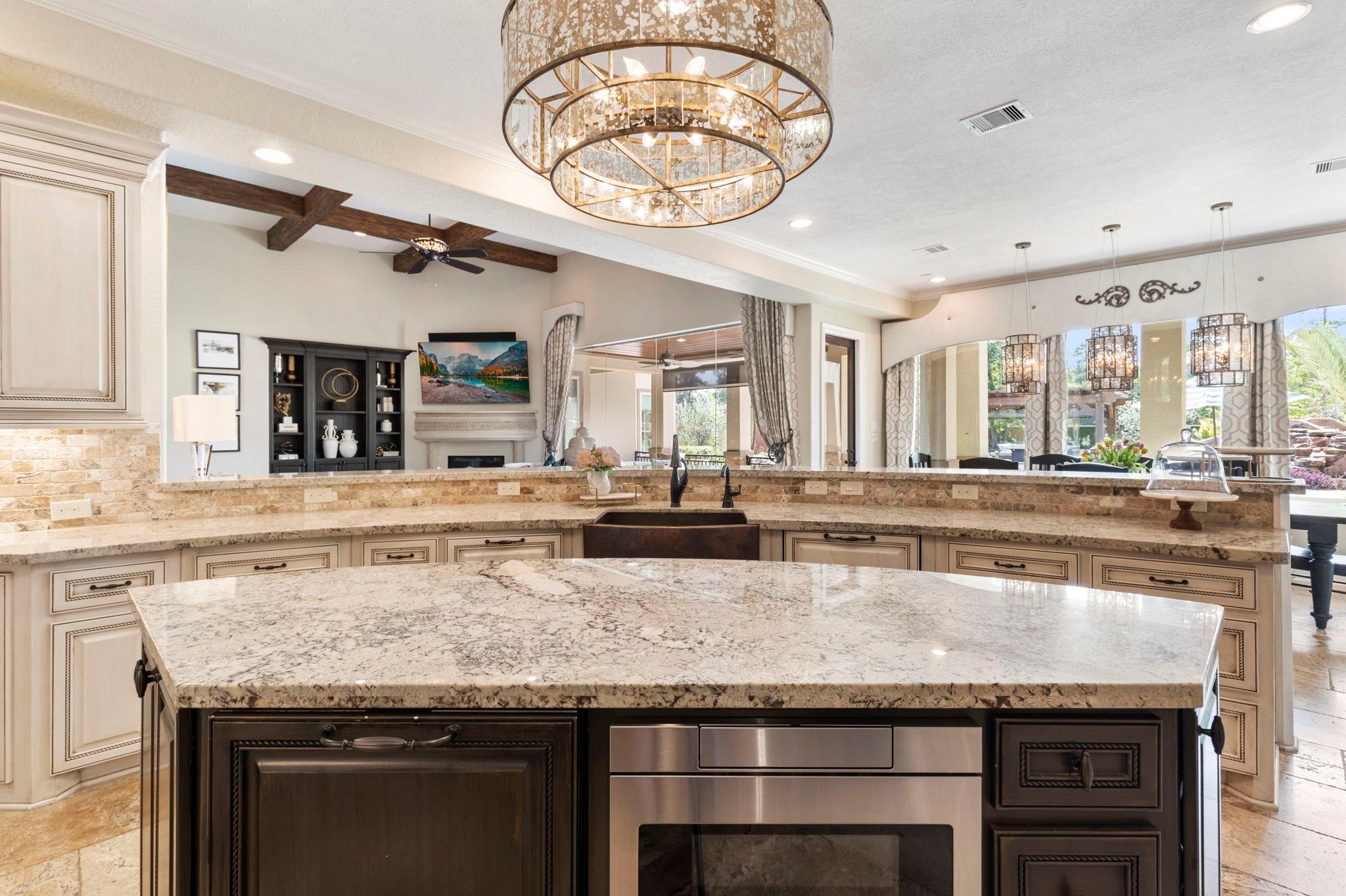 Spacious kitchen with a granite island, dark cabinetry, stainless-steel oven, and open-plan living area.