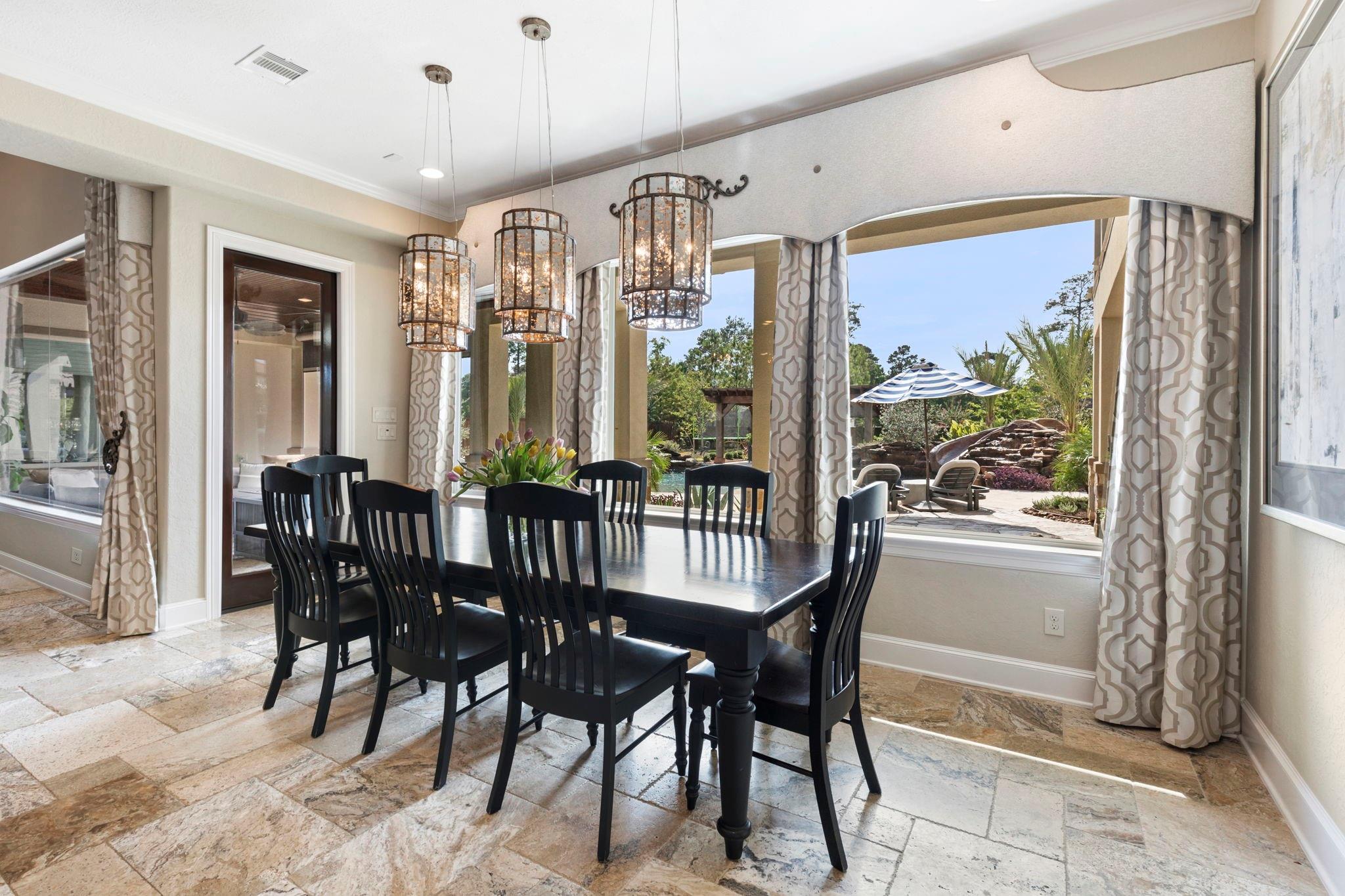 Dining room with a dark wood table and pendant lights overlooking a backyard pool.