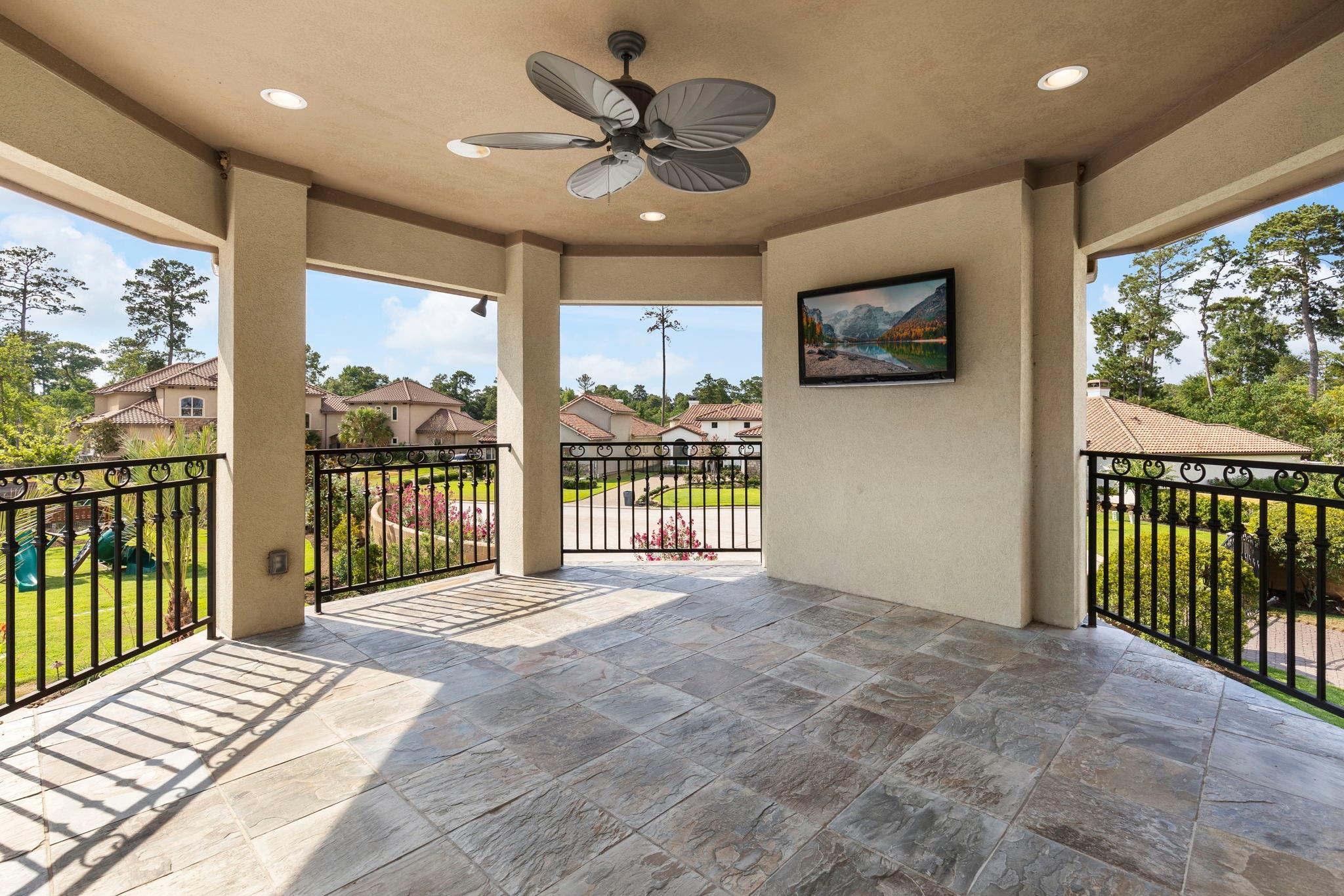 Covered patio with stone tile floors, ceiling fan, television, and views of neighboring homes.