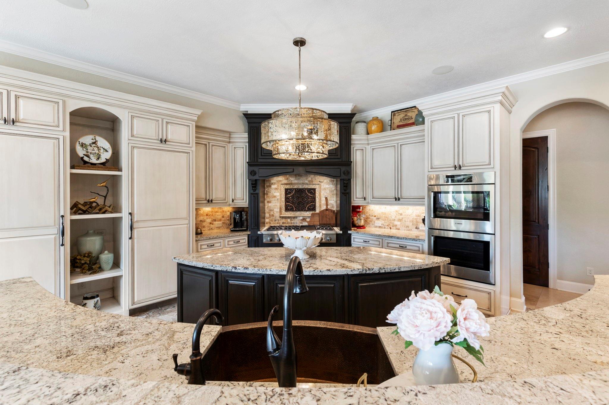 Kitchen with cream cabinetry, dark island, granite counters, and a decorative range hood.